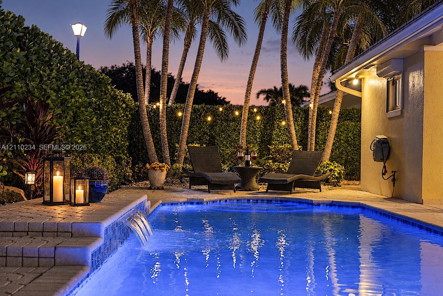 In-ground swimming pool featuring a tiered stone paver deck, integrated water feature, and mature palm trees In-ground swimming pool featuring a tiered stone paver deck, integrated water feature, and mature palm trees