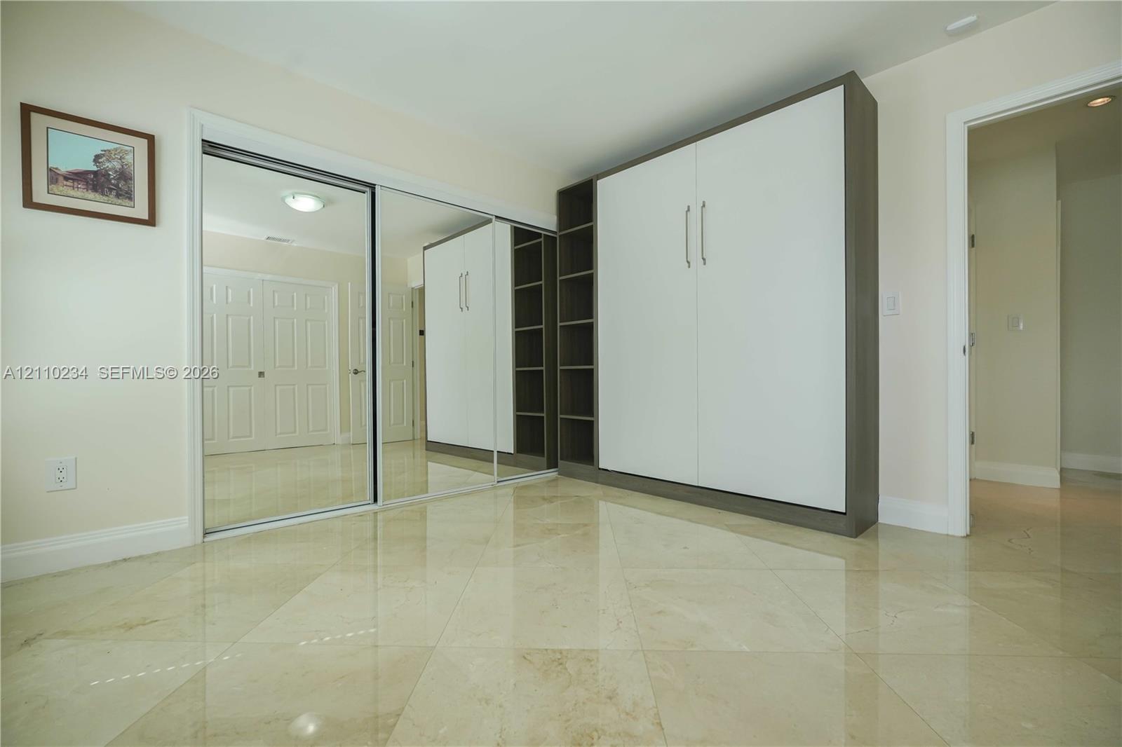 Polished stone flooring, floor-to-ceiling mirrored closet doors, and custom built-in cabinetry featuring integrated shelving and panel-front storage