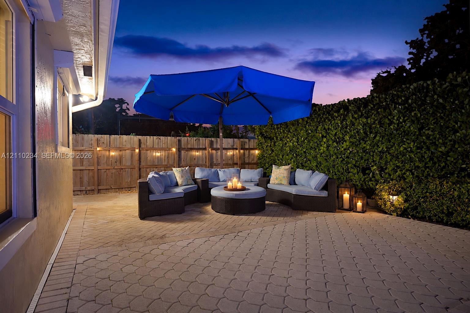 Rear patio featuring concrete pavers, wood perimeter fencing, and dense shrubbery screening