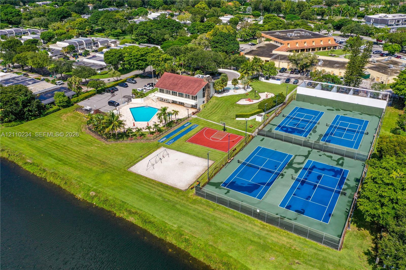 Recreational complex featuring two fenced tennis courts, a basketball court, an outdoor swimming pool, and a sand playground area