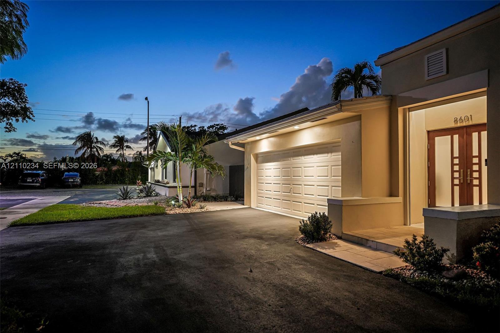 Exterior facade featuring a multi-panel garage door, paved driveway, and double-entry doors with glass inserts