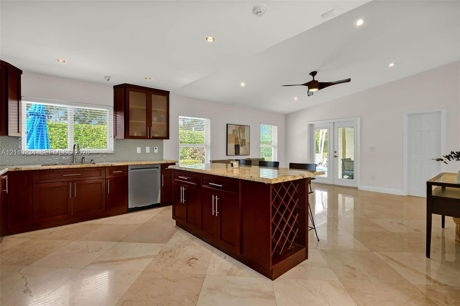 Kitchen featuring dark-toned cabinetry, a central island with built-in wine storage, stone countertops, large-format tile flooring, and a vaulted ceiling with a recessed ceiling fan