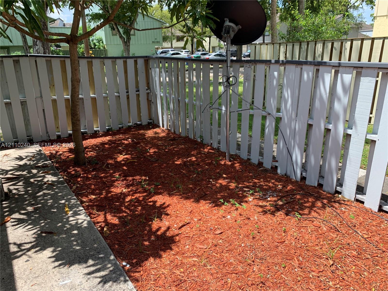 Enclosed outdoor area featuring a wood-panel fence, concrete patio, mulch ground cover, and a mature tree