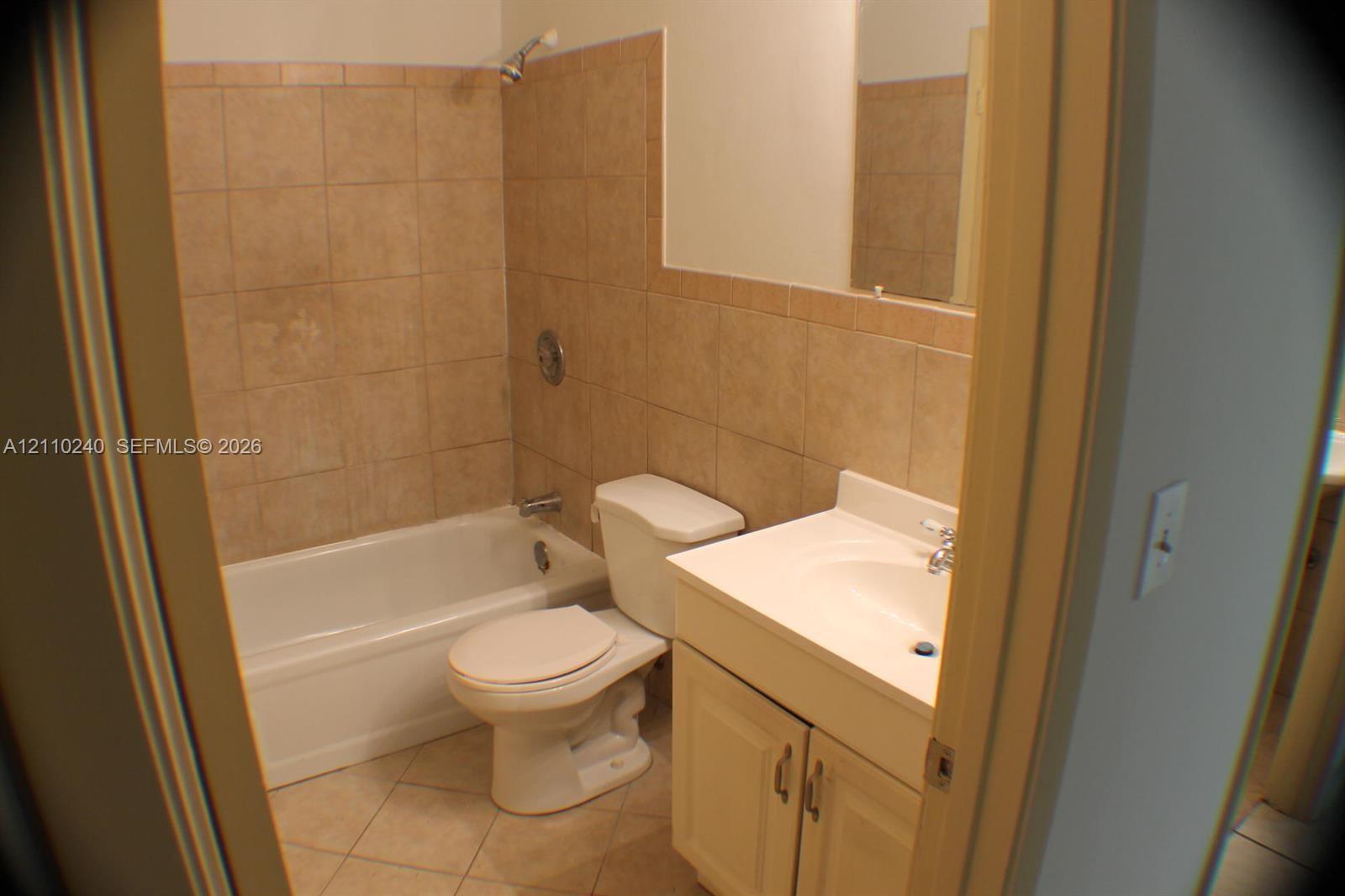 Bathroom featuring a tub-shower combination with floor-to-ceiling tile surround, white vanity cabinet with an integrated sink, wall-mounted mirror, and tile flooring