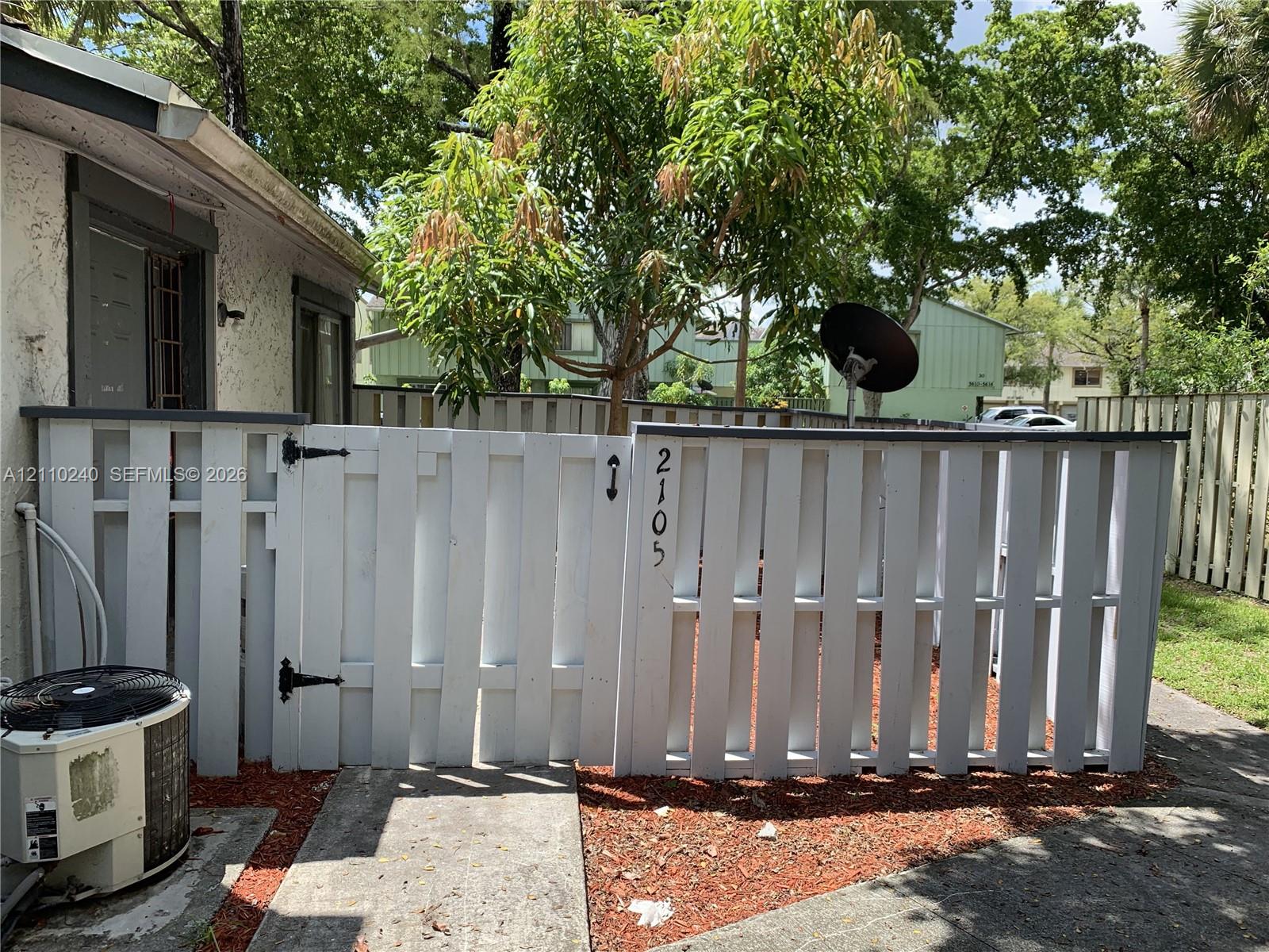Stucco exterior featuring a white vertical picket fence, a gated entry, and a concrete pathway