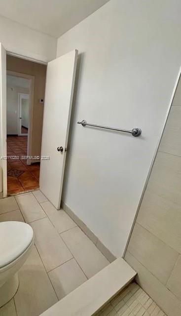 Bathroom featuring neutral large-format floor tiling, a walk-in shower with light-toned wall tile, and a wall-mounted metal towel bar