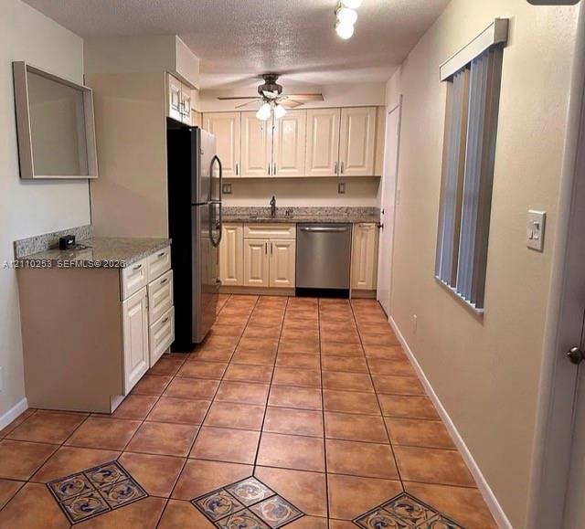 Kitchen featuring cream cabinetry, stone-finish countertops, stainless steel appliances, and ceramic tile flooring with decorative inlay accents