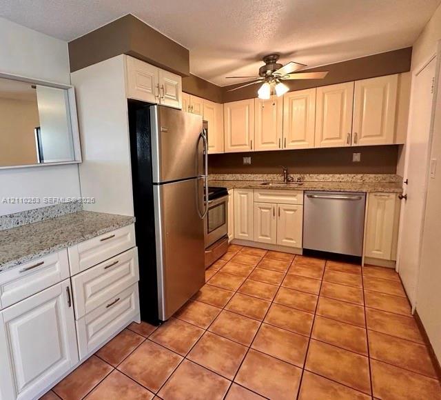 Kitchen featuring off-white cabinetry, speckled stone-finish countertops, stainless steel appliances, and ceramic tile flooring