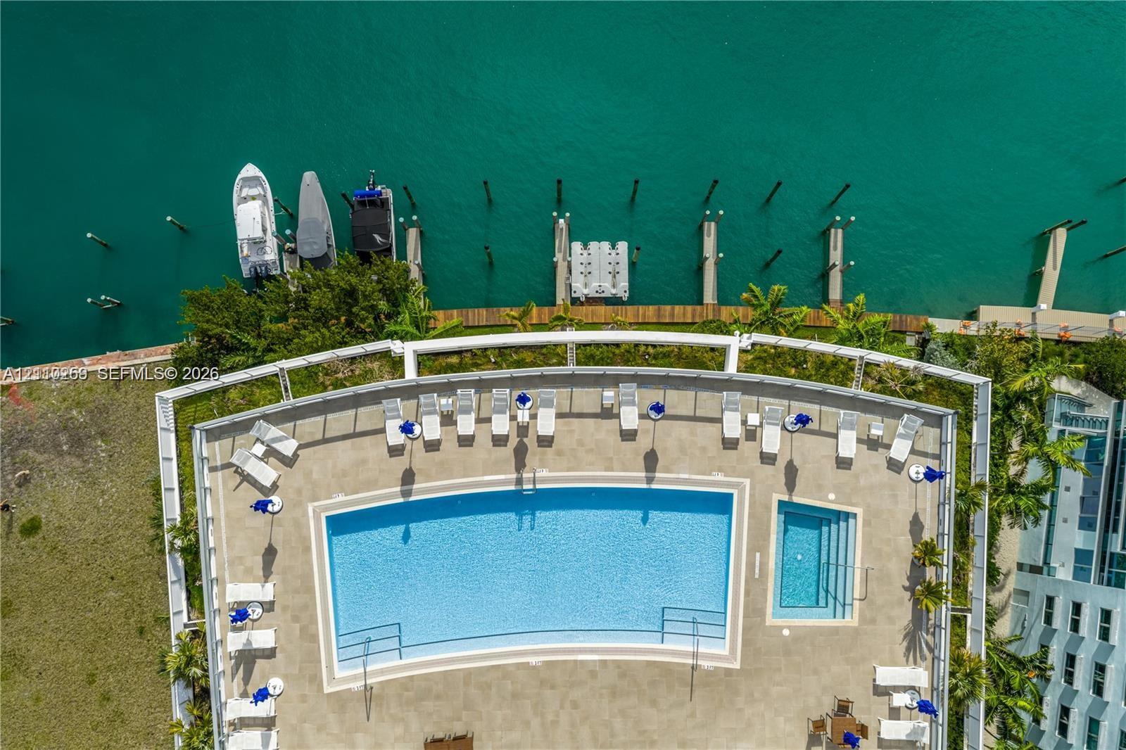 Waterfront pool deck featuring a swimming pool, attached spa, paved terrace, and protective glass railing