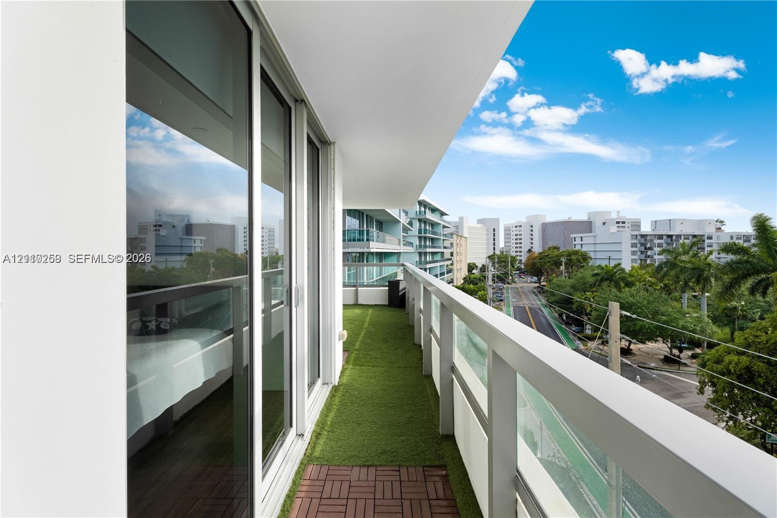 Covered balcony with a glass-paneled railing, synthetic turf flooring, and floor-to-ceiling sliding glass doors