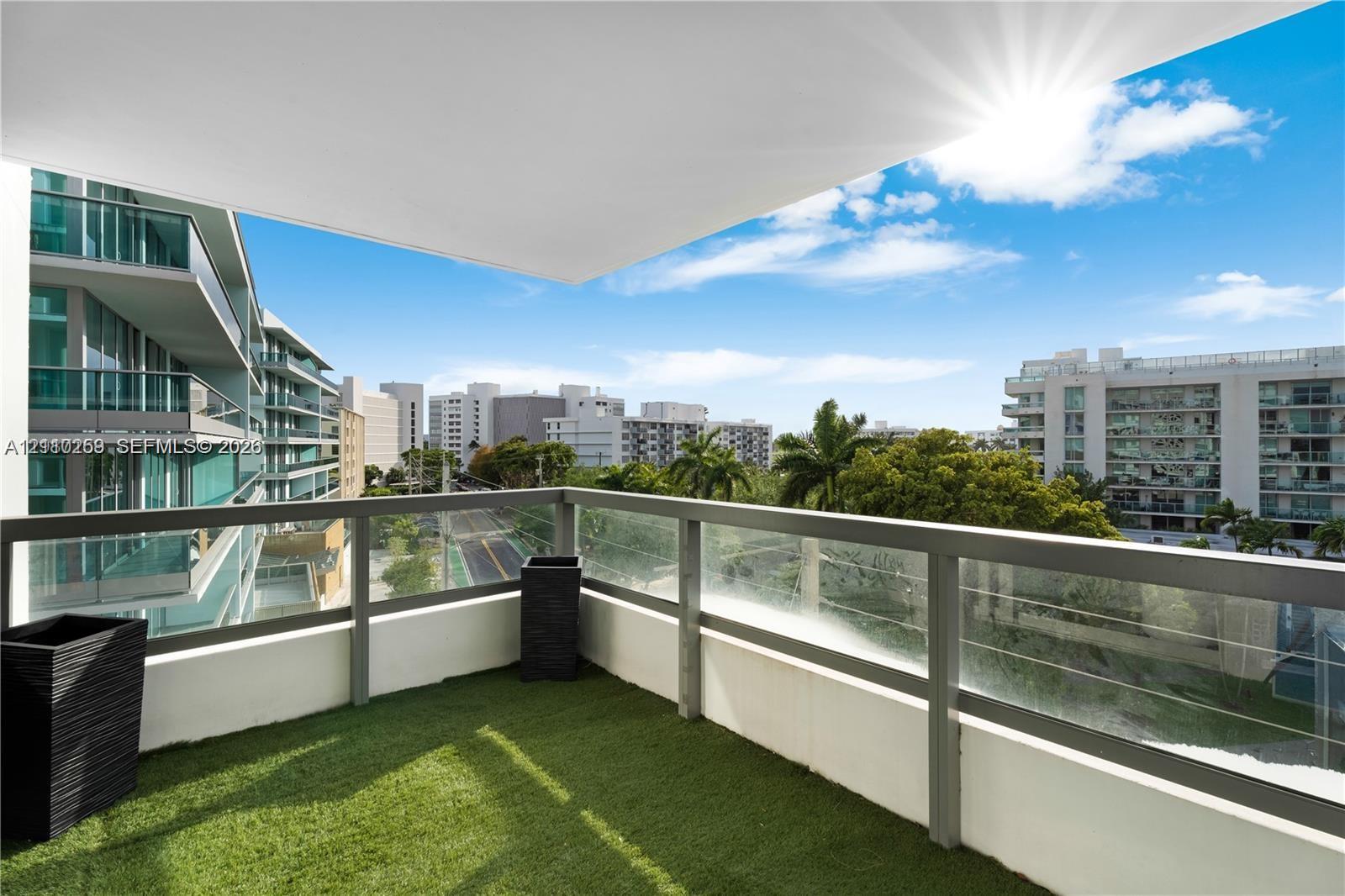 Covered balcony featuring green turf flooring and a glass panel railing