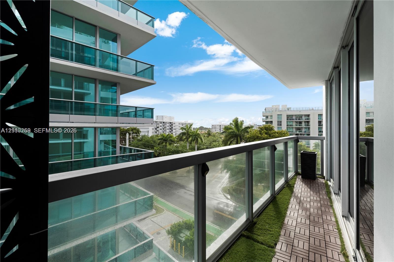 Private balcony featuring glass panel railings, decorative screen detailing, and a combination of paved and turf surfacing