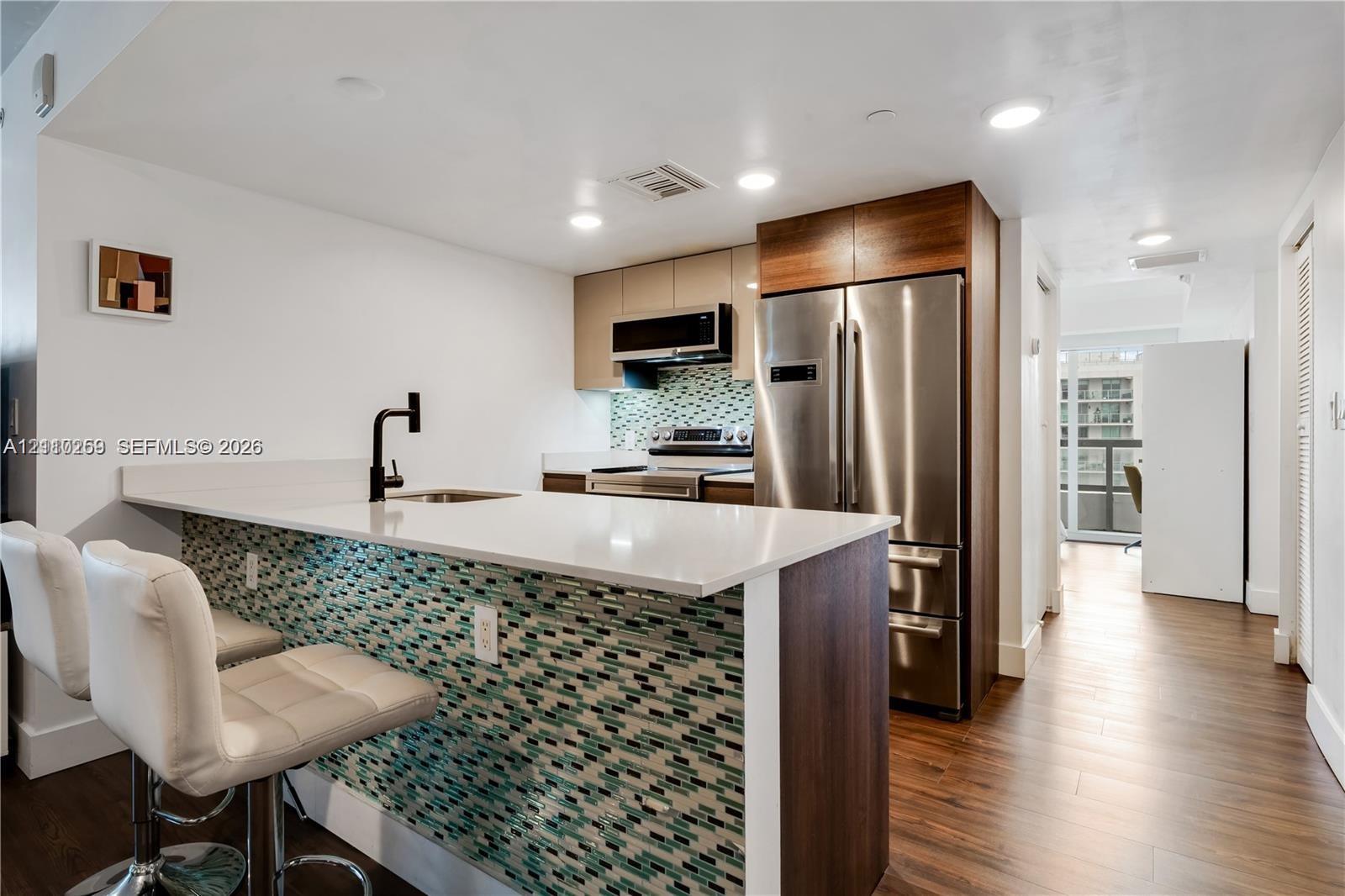 Kitchen featuring a breakfast bar with a solid surface countertop, wood-finish flooring, stainless steel appliances, and a glass-tile backsplash