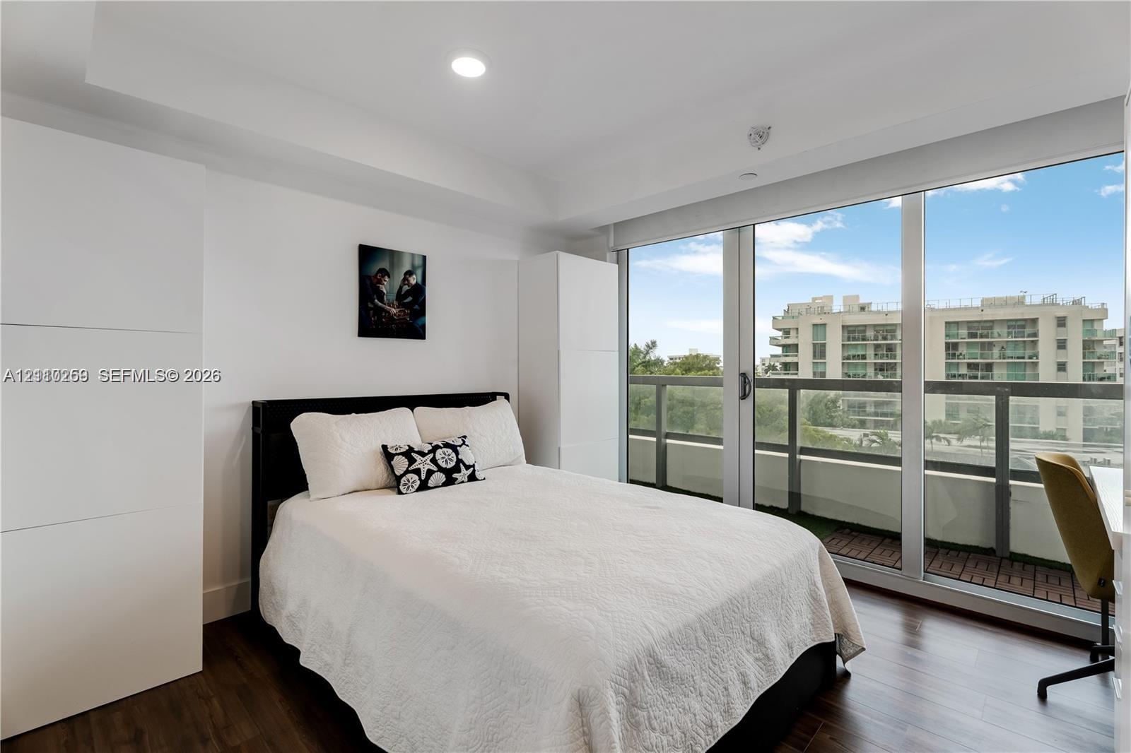 Floor-to-ceiling glass sliding doors, dark wood-finish flooring, recessed lighting, and a private balcony with metal railings