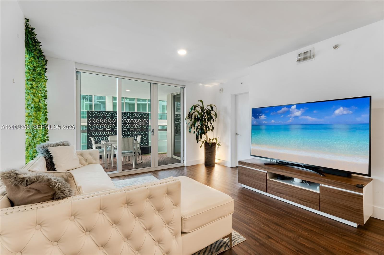 Open-concept living space featuring wood-finish flooring, floor-to-ceiling glass sliding doors, and a private balcony with decorative privacy screening