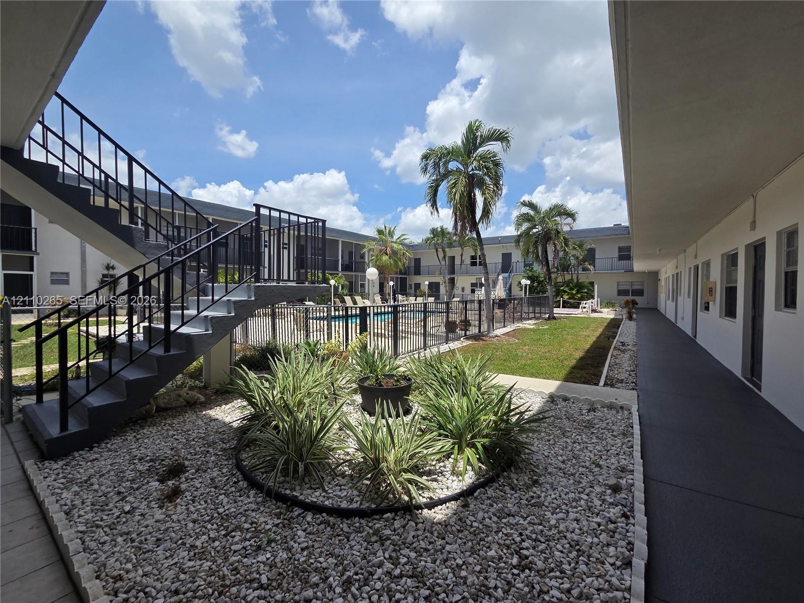 Courtyard featuring an outdoor swimming pool with metal perimeter fencing, landscaped rock gardens with native vegetation, palm trees, and metal staircases