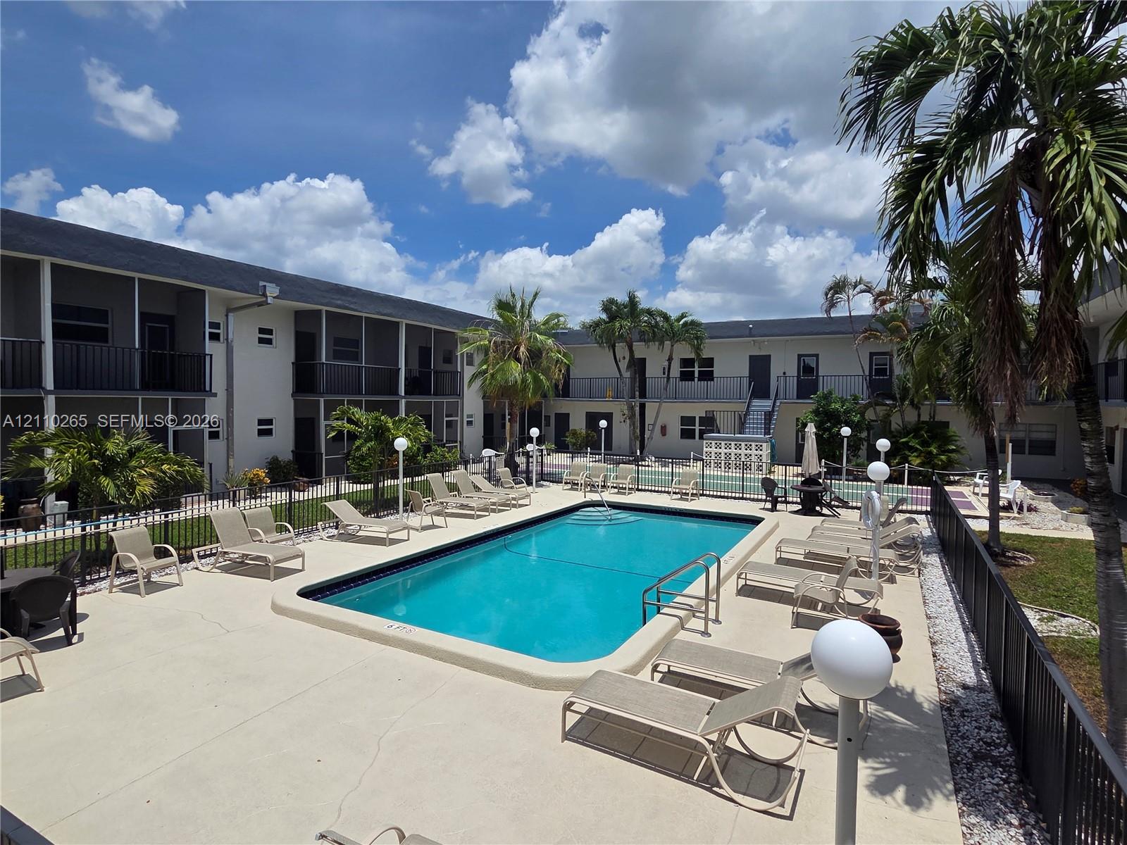 Outdoor swimming pool featuring a concrete deck, decorative perimeter fencing, and mature palm trees