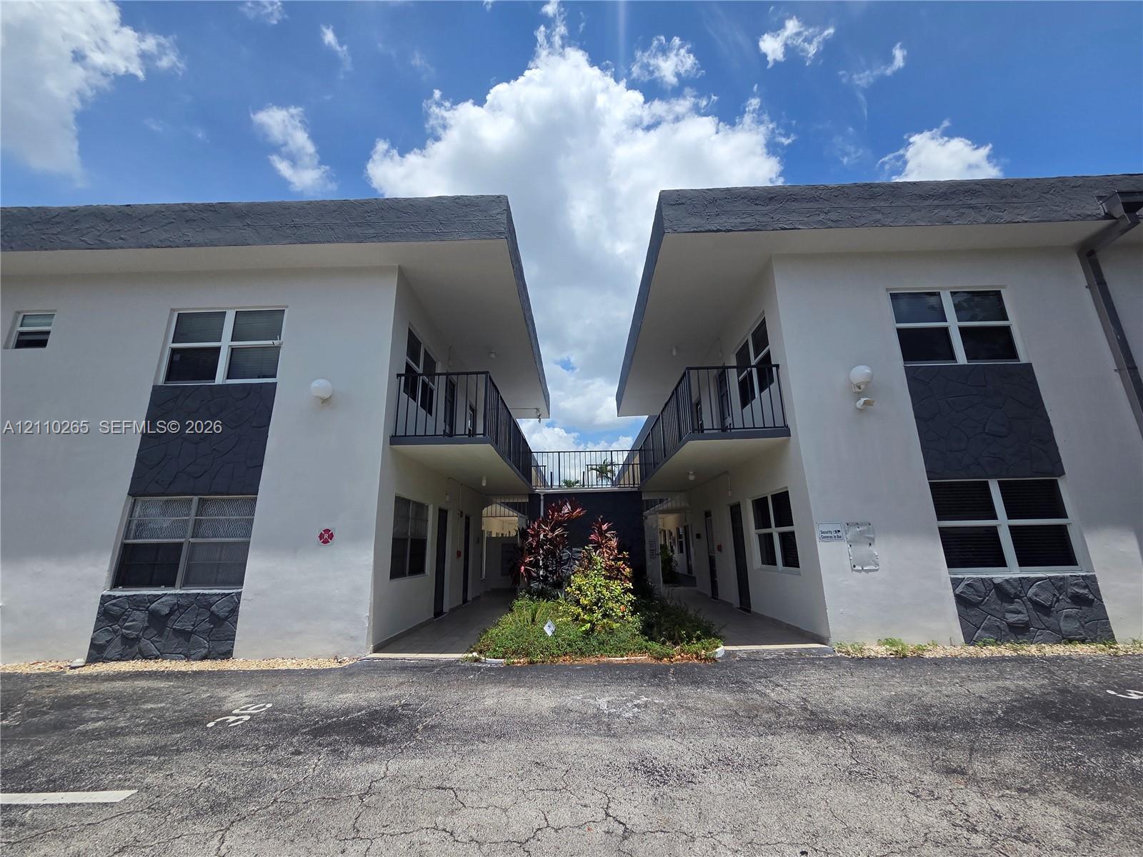 Two-story exterior featuring white stucco facades, dark stone veneer accents, flat rooflines, and metal balcony railings