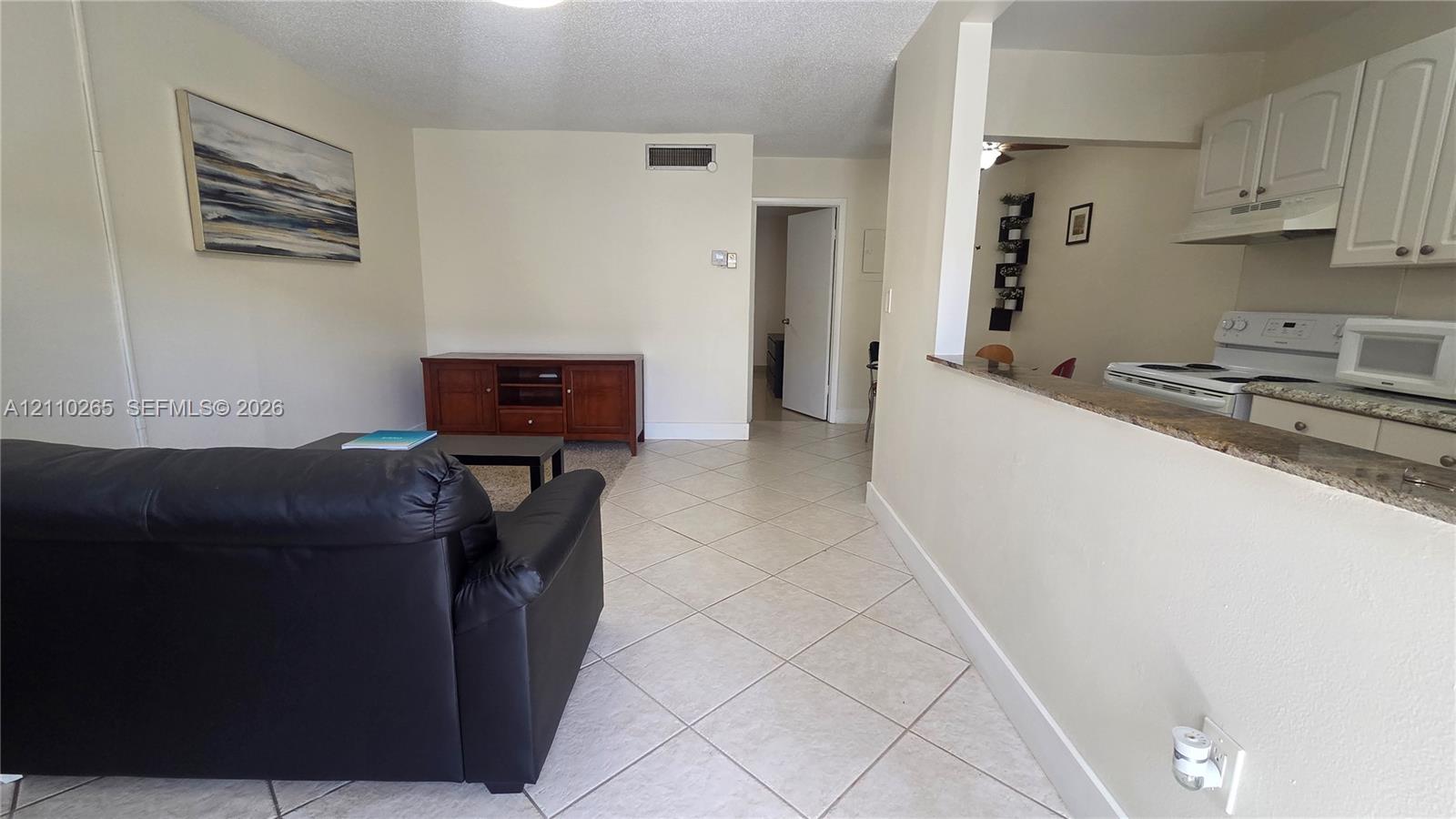 Interior featuring diagonal ceramic tile flooring, kitchen pass-through window with a stone-finish countertop, and white shaker-style cabinetry