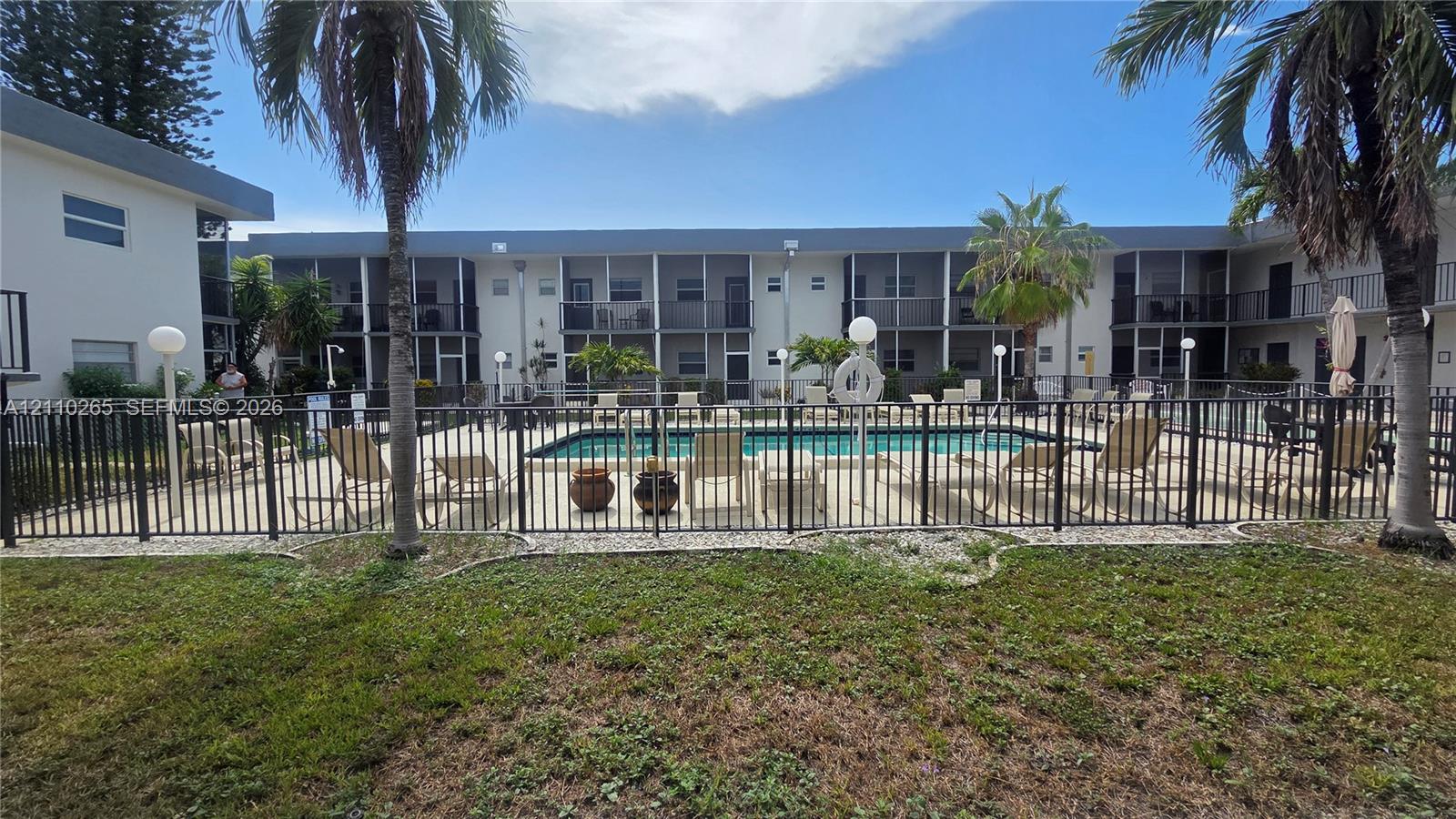 Swimming pool area featuring a metal security fence, paved perimeter, and mature palm trees