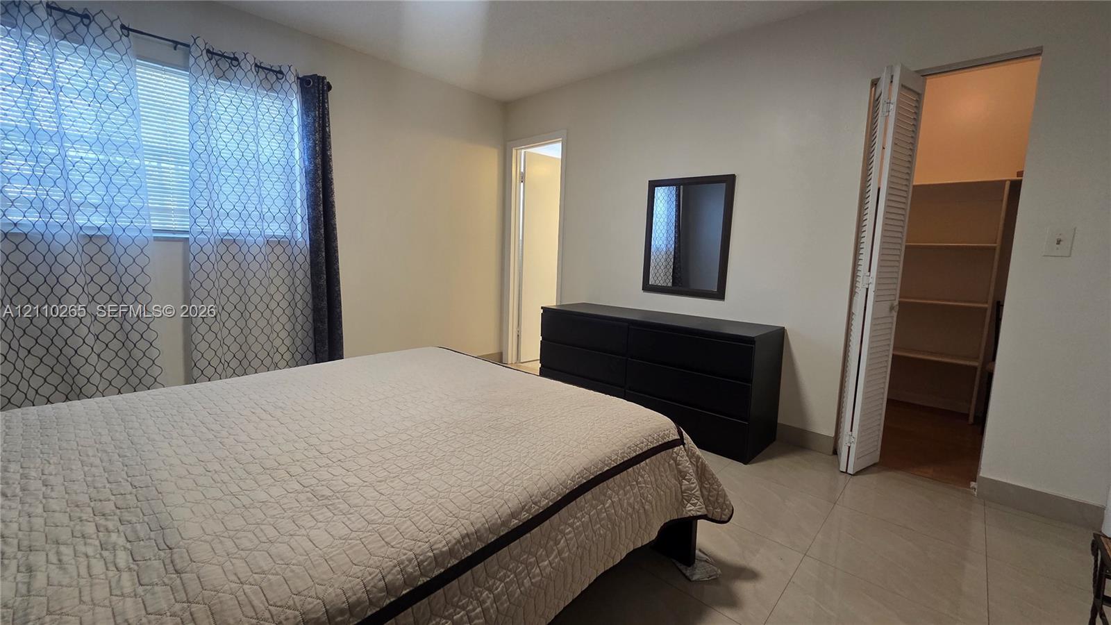 Neutral wall tones, horizontal window blinds, large-format tile flooring, and walk-in closet featuring built-in shelving