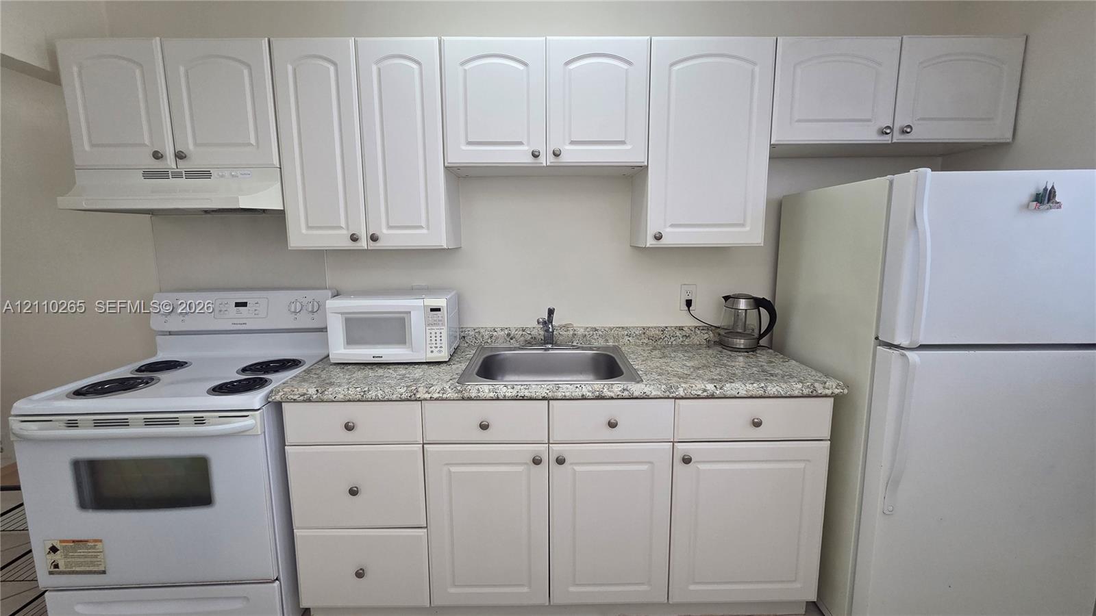 Kitchen area featuring white shaker-style cabinetry, stone-finish countertops, stainless steel sink with a chrome faucet, and white electric range