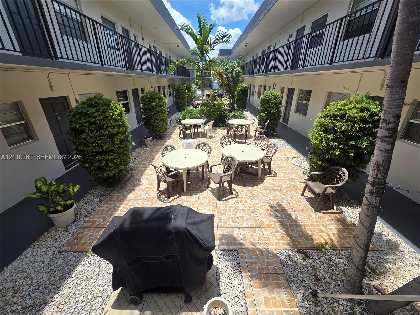 Courtyard featuring paved tile patio, ornamental shrubbery, decorative stone ground cover, and palm trees