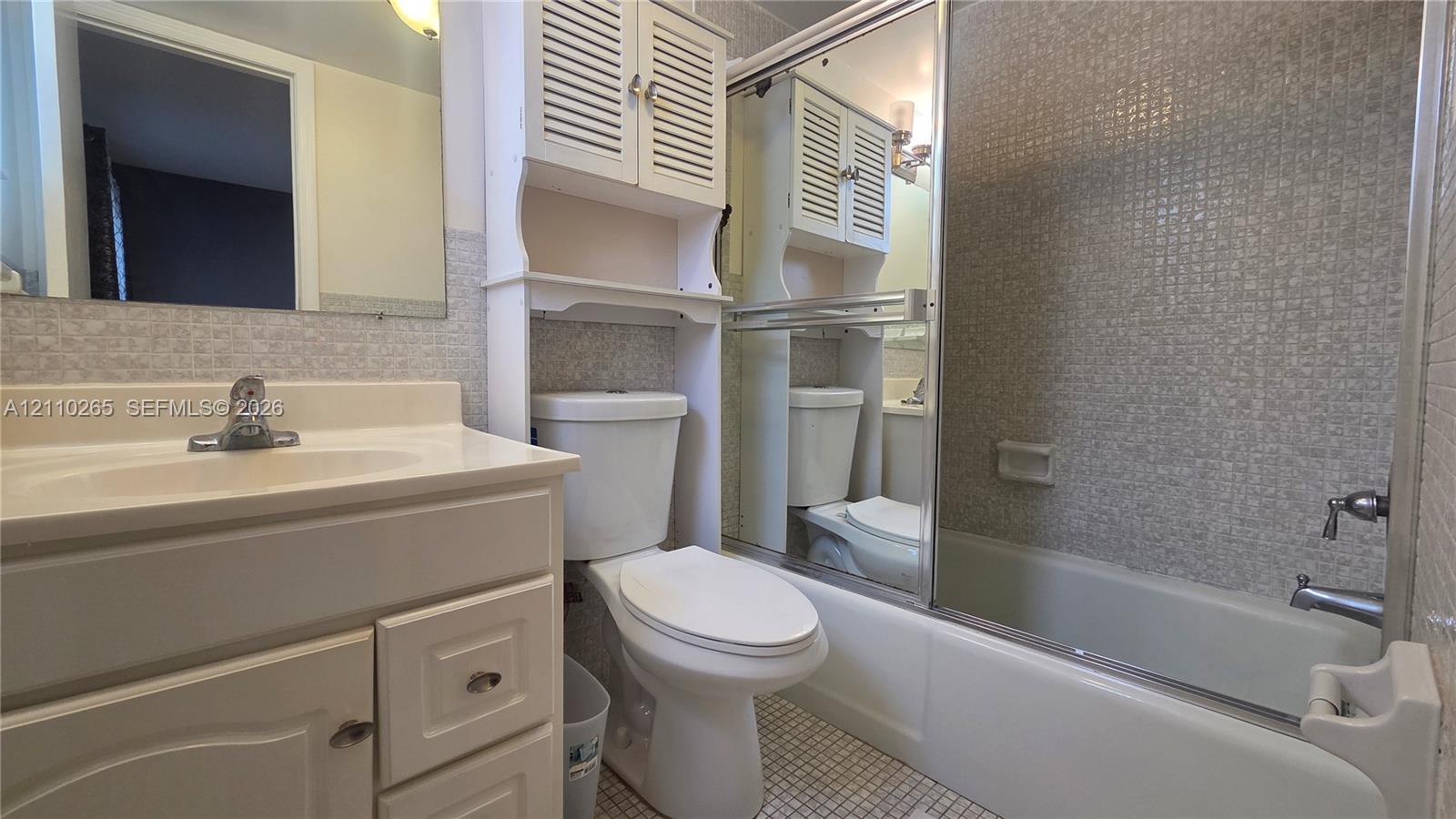 Bathroom featuring a vanity with integrated sink, built-in over-the-toilet storage cabinetry, mirrored sliding shower enclosure, and mosaic-tiled shower surround