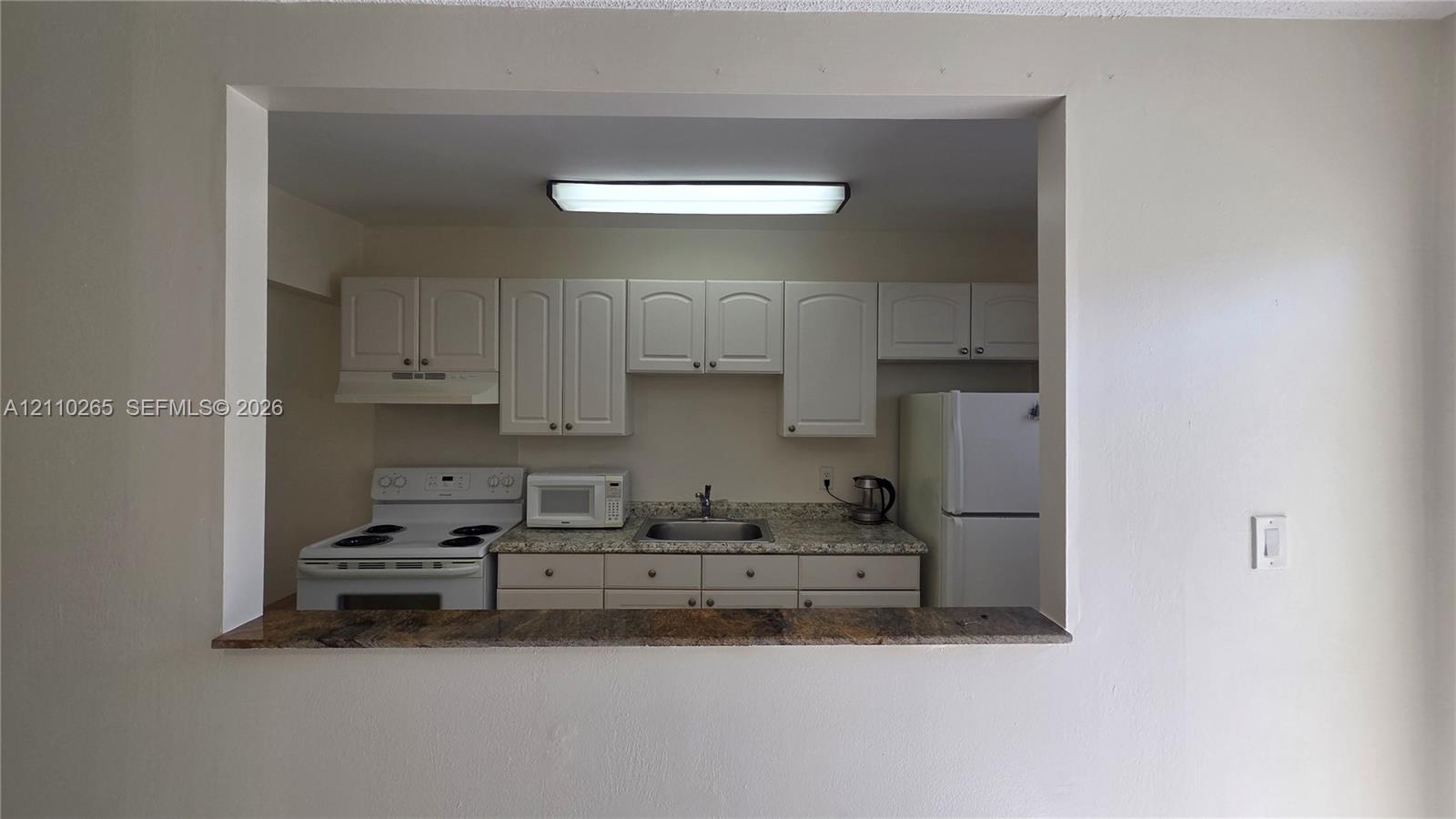 Kitchen featuring white cabinetry, stone-finish countertops, stainless steel sink, and built-in pass-through counter