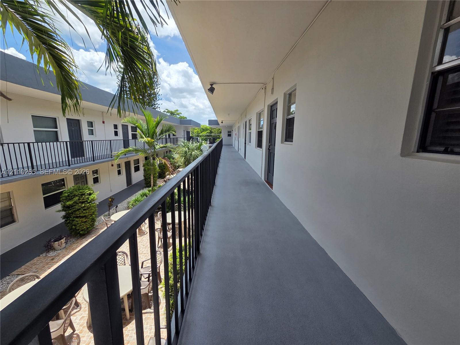 Exterior corridor featuring a smooth concrete walkway, black metal railings, and recessed ceiling lighting