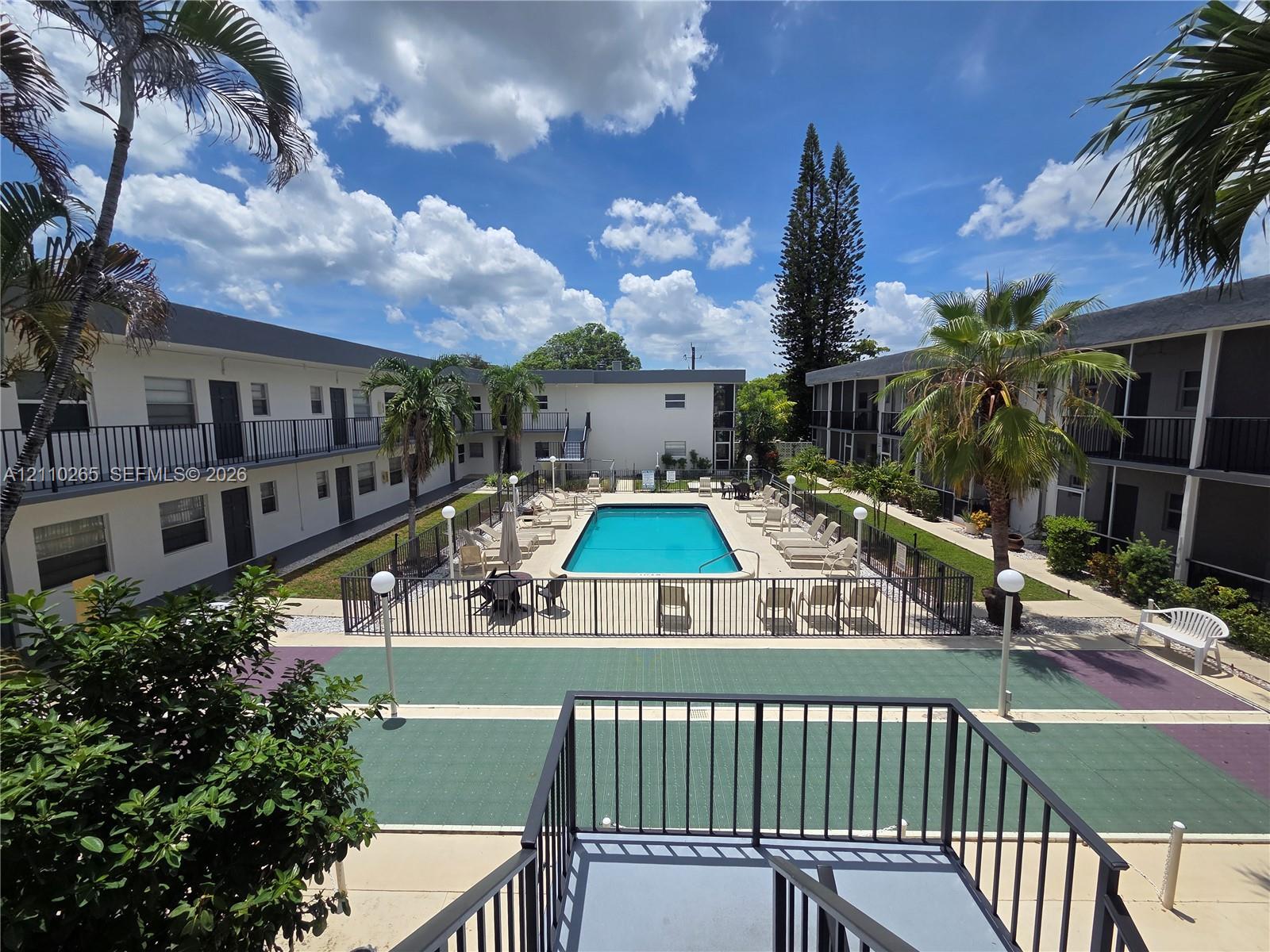 Courtyard featuring an in-ground swimming pool, fenced pool deck, paved recreational space, and mature palm trees