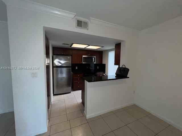 Kitchen featuring dark wood cabinetry, stainless steel appliances, black countertops, and tile flooring