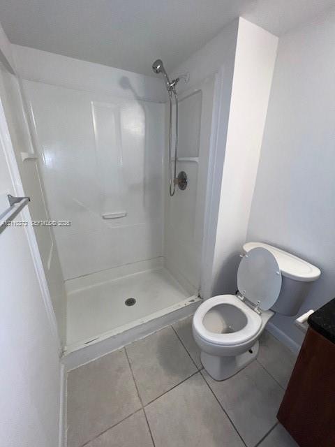 Full-height shower enclosure with a handheld showerhead, two-piece toilet, and tile flooring