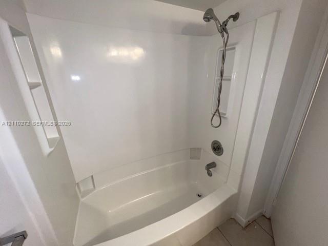 Bathtub and shower combination featuring a glossy white surround, integrated shelving niches, and a polished metallic handheld shower fixture