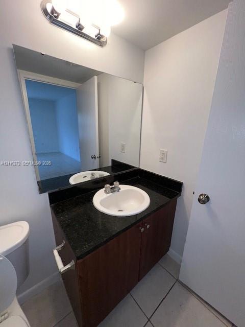 Vanity featuring a dark stone countertop, integrated undermount sink, dual-door wood-finish cabinetry, and a large-format vanity mirror with an overhead light fixture