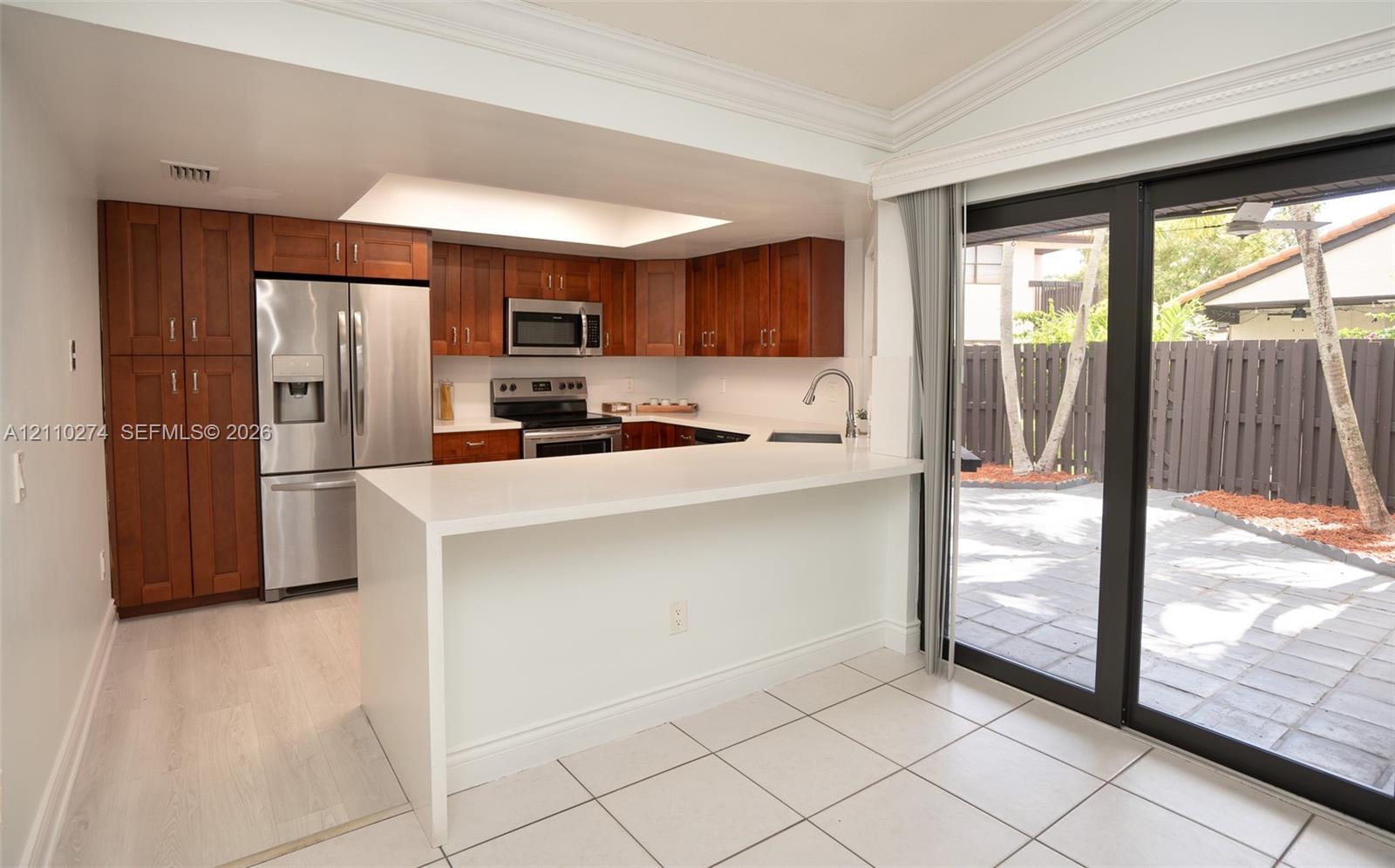 Kitchen featuring wood cabinetry, stainless steel appliances, white quartz countertops with a waterfall edge, recessed lighting, and sliding glass doors opening to a paved patio