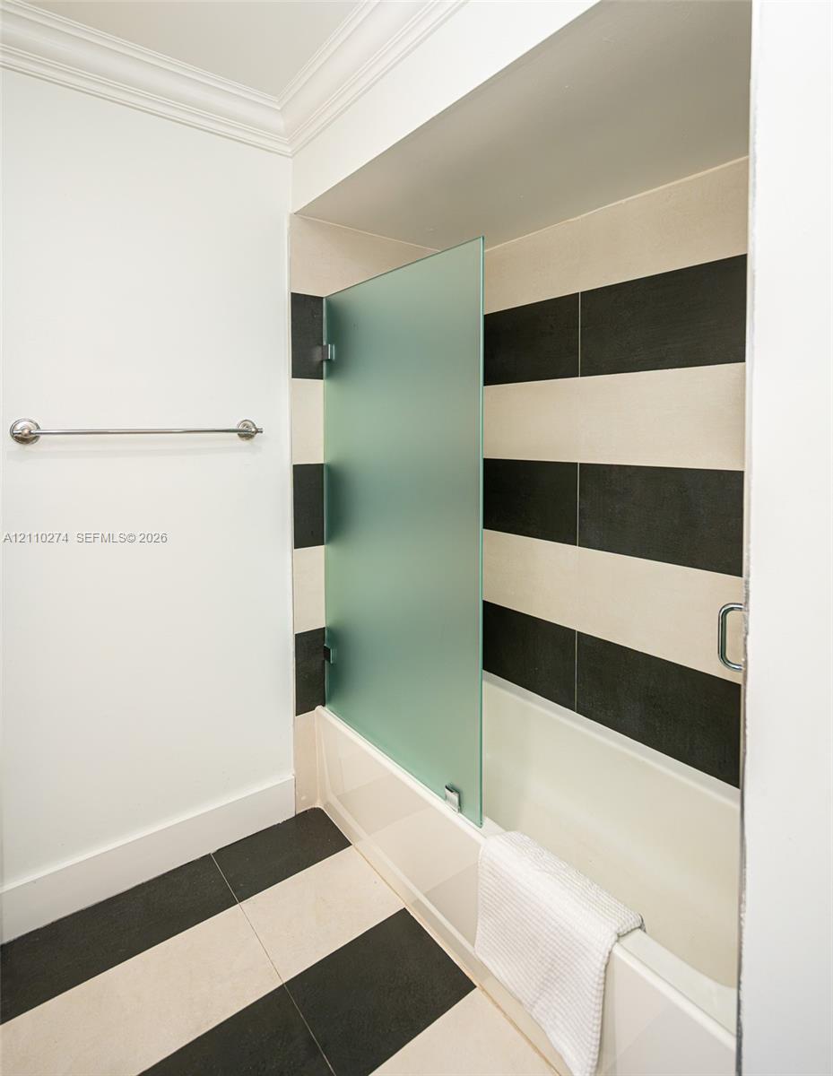 Bathtub featuring a frosted glass panel, high-contrast horizontal tile wall surround, and large-format two-tone floor tiling