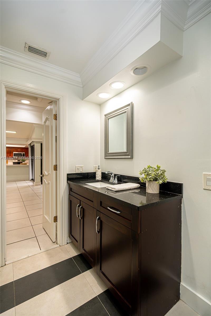 Dark wood vanity featuring a polished stone countertop, integrated sink, recessed lighting, and crown molding
