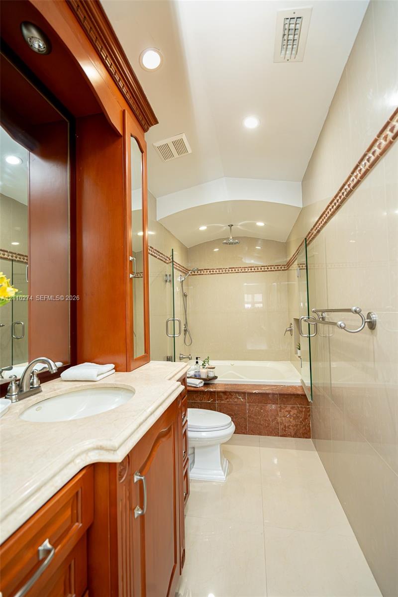 Bathroom featuring a wood-finish vanity with a stone countertop, an integrated jetted tub with stone tile surround, a glass-enclosed shower, and polished tile flooring