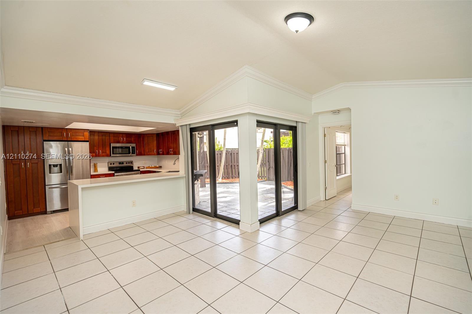 Kitchen featuring wood cabinetry, stainless steel appliances, and a breakfast bar, with vaulted ceilings and sliding glass doors opening to a paved exterior space Kitchen featuring wood cabinetry, stainless steel appliances, and a breakfast bar, with vaulted ceilings and sliding glass doors opening to a paved exterior space