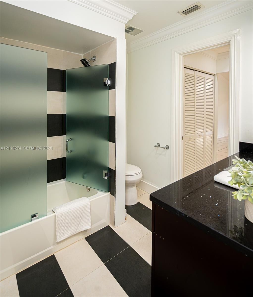 Bathroom featuring a vanity with a dark stone countertop, bathtub with a frosted glass enclosure, and a black-and-white tiled floor