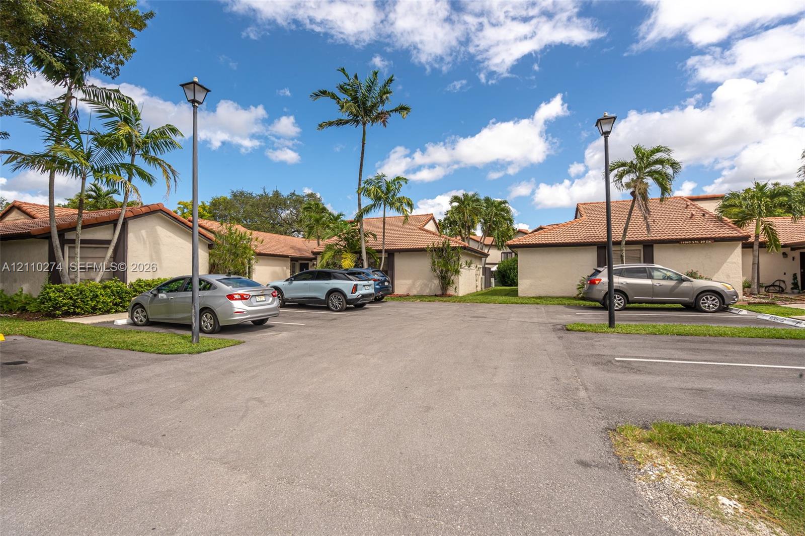 Single-story building exteriors featuring stucco facades, multi-pitched tile roofing, dedicated surface parking, and mature palm landscaping with integrated pole lighting