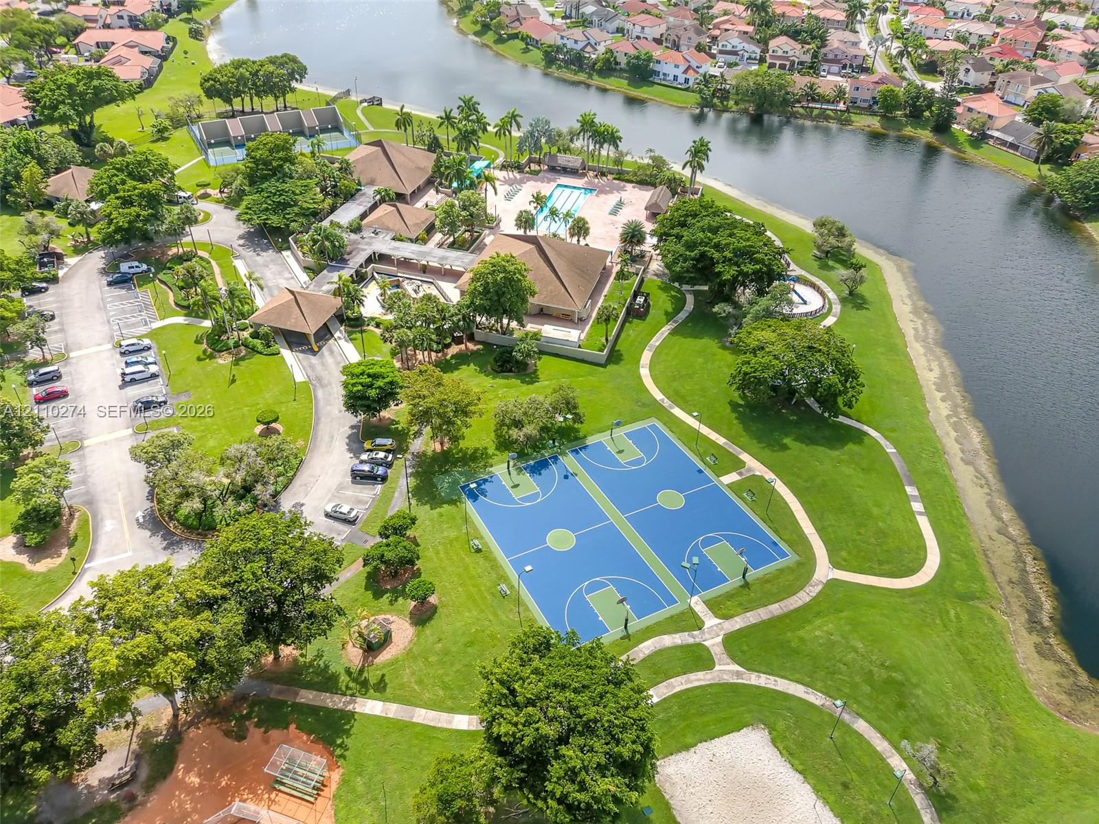 Community recreational area featuring dual basketball courts, a swimming pool, winding paved pathways, and waterfront access