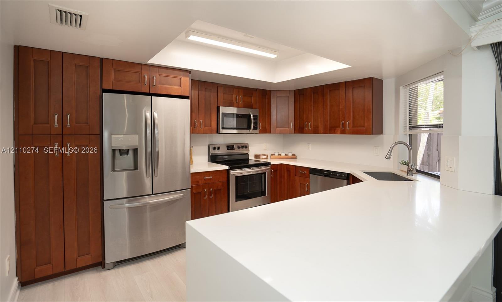 Kitchen featuring warm-toned wood cabinetry, stainless steel appliances, solid surface countertops, a recessed ceiling fixture, and a single-basin undermount sink