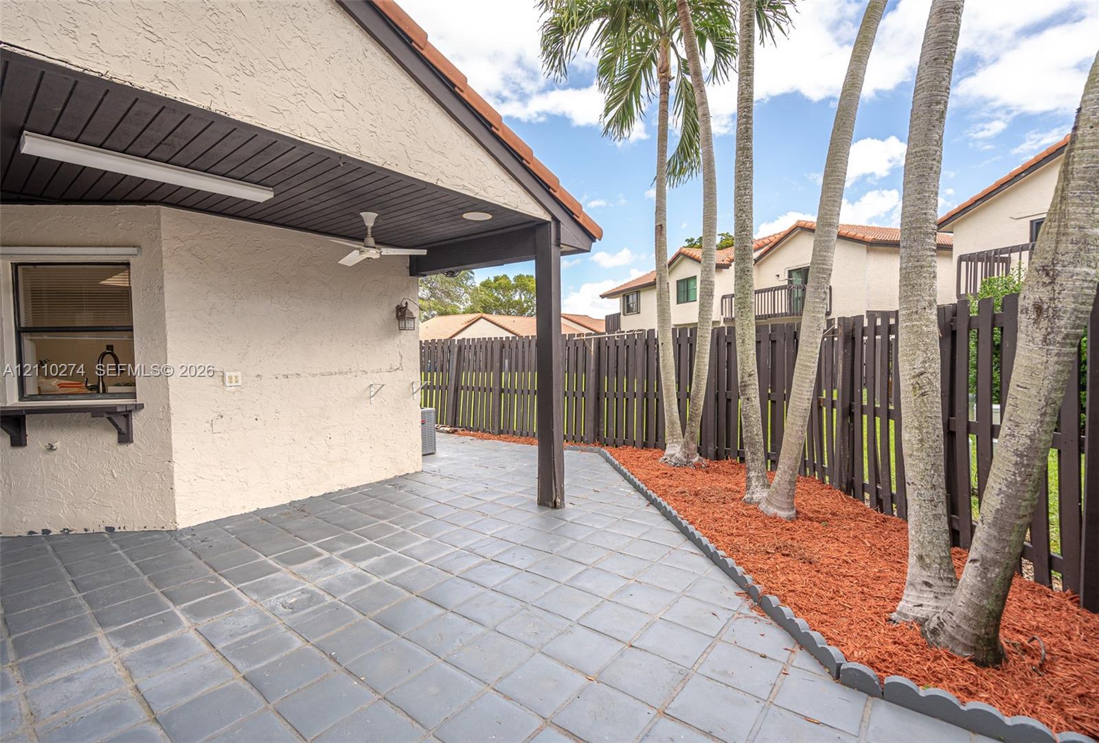 Covered outdoor patio featuring tile flooring, a built-in service window, a ceiling fan, and a wood-slat perimeter fence