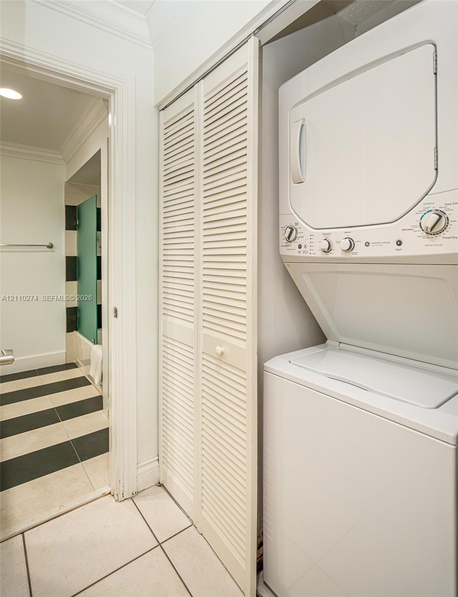 Laundry area featuring a stacked washer and dryer unit, white louvered bifold closet doors, and large-format tile flooring with a black and white striped pattern