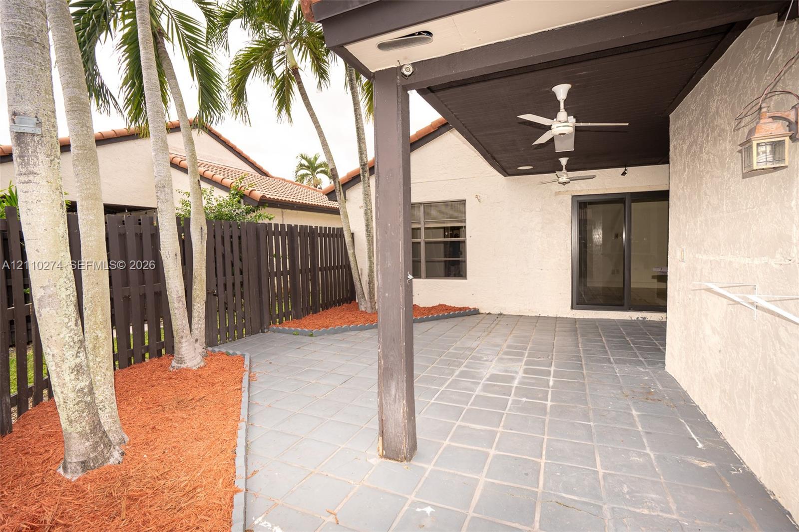 Covered patio with tile flooring, ceiling fans, integrated wall-mounted exterior lighting, and wood-slat fencing