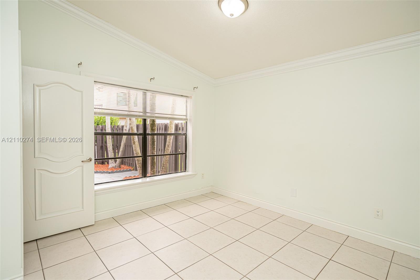 Room featuring vaulted ceilings, crown molding, large format tile flooring, and a multi-pane window with a black frame