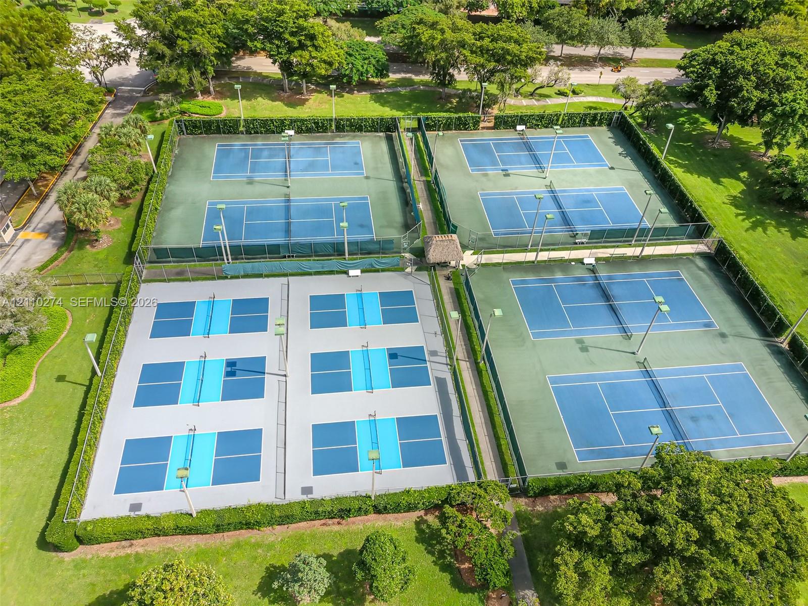 Outdoor recreation area featuring two dual-court tennis facilities, two multi-court pickleball setups, perimeter fencing, and manicured landscaping
