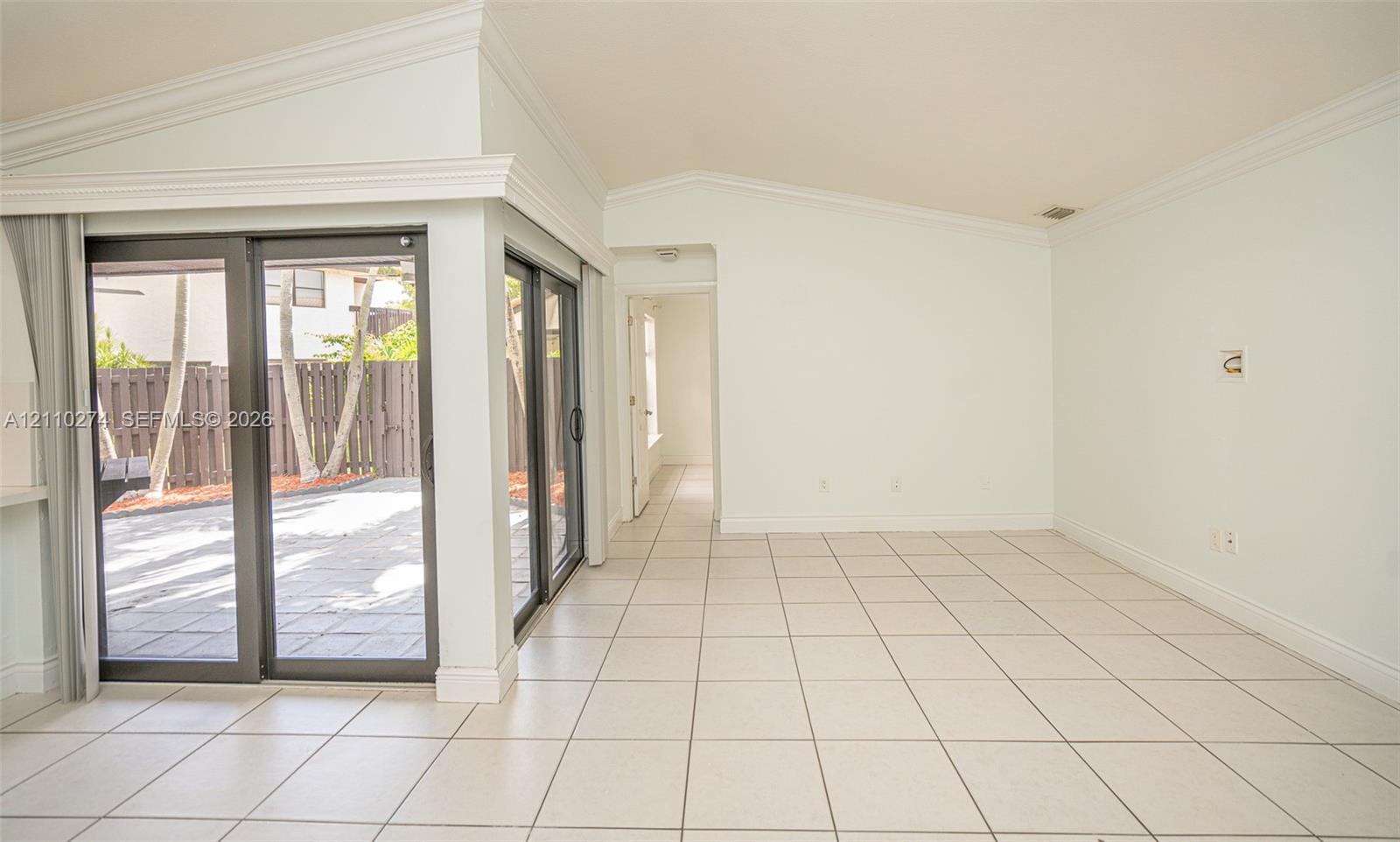 Vaulted ceiling featuring crown molding, ceramic tile flooring, and sliding glass doors with dark frames